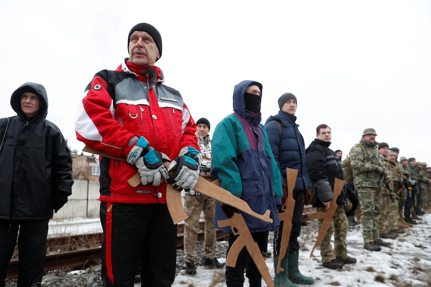Men with replica wooden rifles stand at attention in snowy conditions in Kyiv.