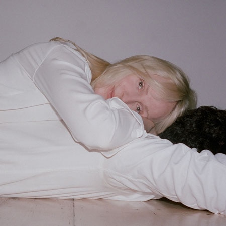 Laura Marling lies on the floor, wearing a white suit, smiling, on the cover of Song For Our Daughter