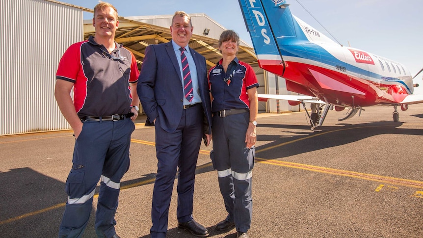 The Chief Executive of Central Operations Tony Vaughan is standing a male and female RFDS crew member in front of a plane