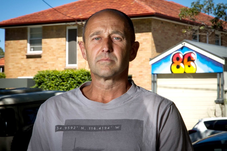 Man stands in front of a boarding house with the number 86 painted on front.