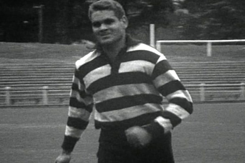 A young football player runs on the field in a striped guernsey.