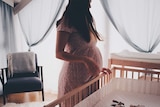 Pregnant woman looking down at empty cot in a story about gender disappointment.
