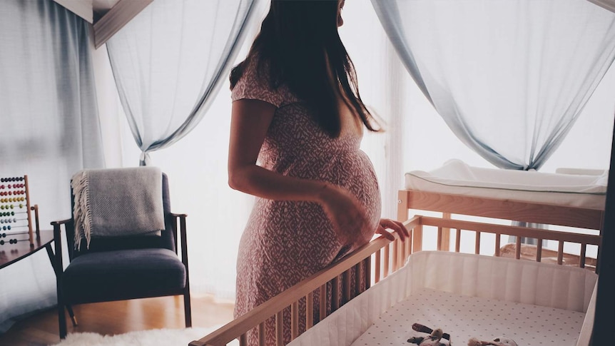 Pregnant woman looking down at empty cot in a story about gender disappointment.