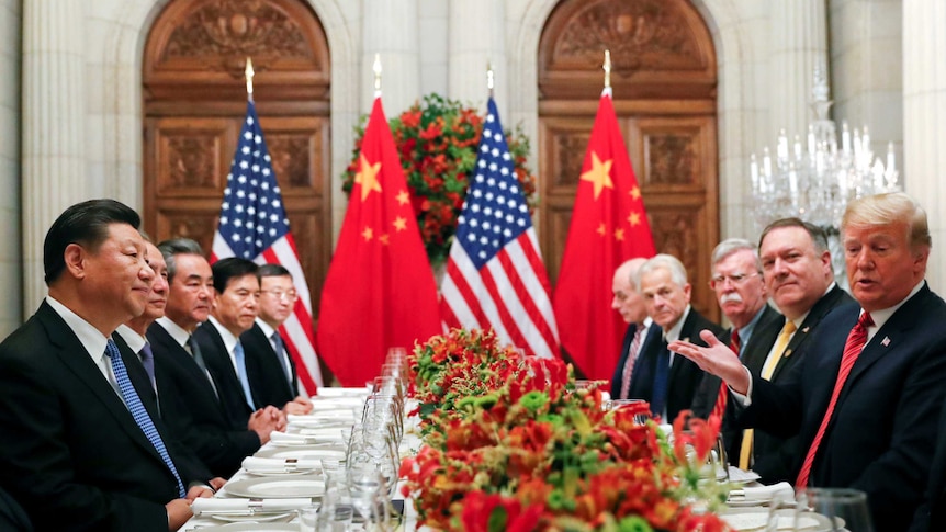 Donald Trump and Xi Jingping sit with US and Chinese officials at a table set for dinner.