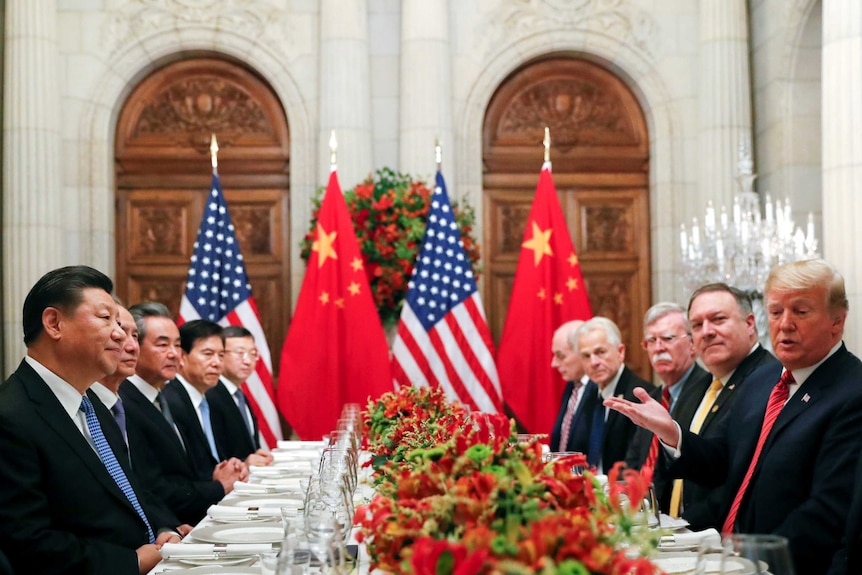 Donald Trump and Xi Jingping sit with US and Chinese officials at a table set for dinner.