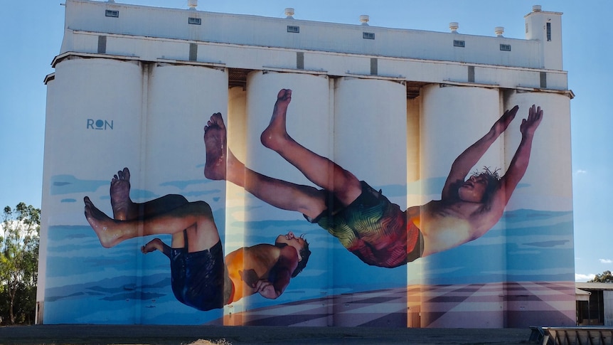 Large silos with a mural of two boys jumping backwards into the water.