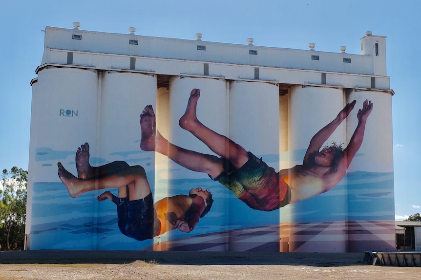 Large silos with a mural of two boys jumping backwards into the water.