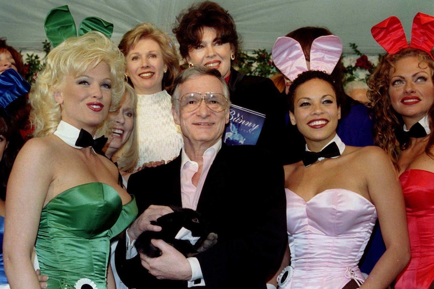 Hugh Hefner surrounded by former and present Playmates, and holding a pet rabbit.