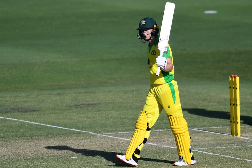 An Australian batter raises her bat with her left arm after scoring a half-century in a women's ODI against New Zealand.