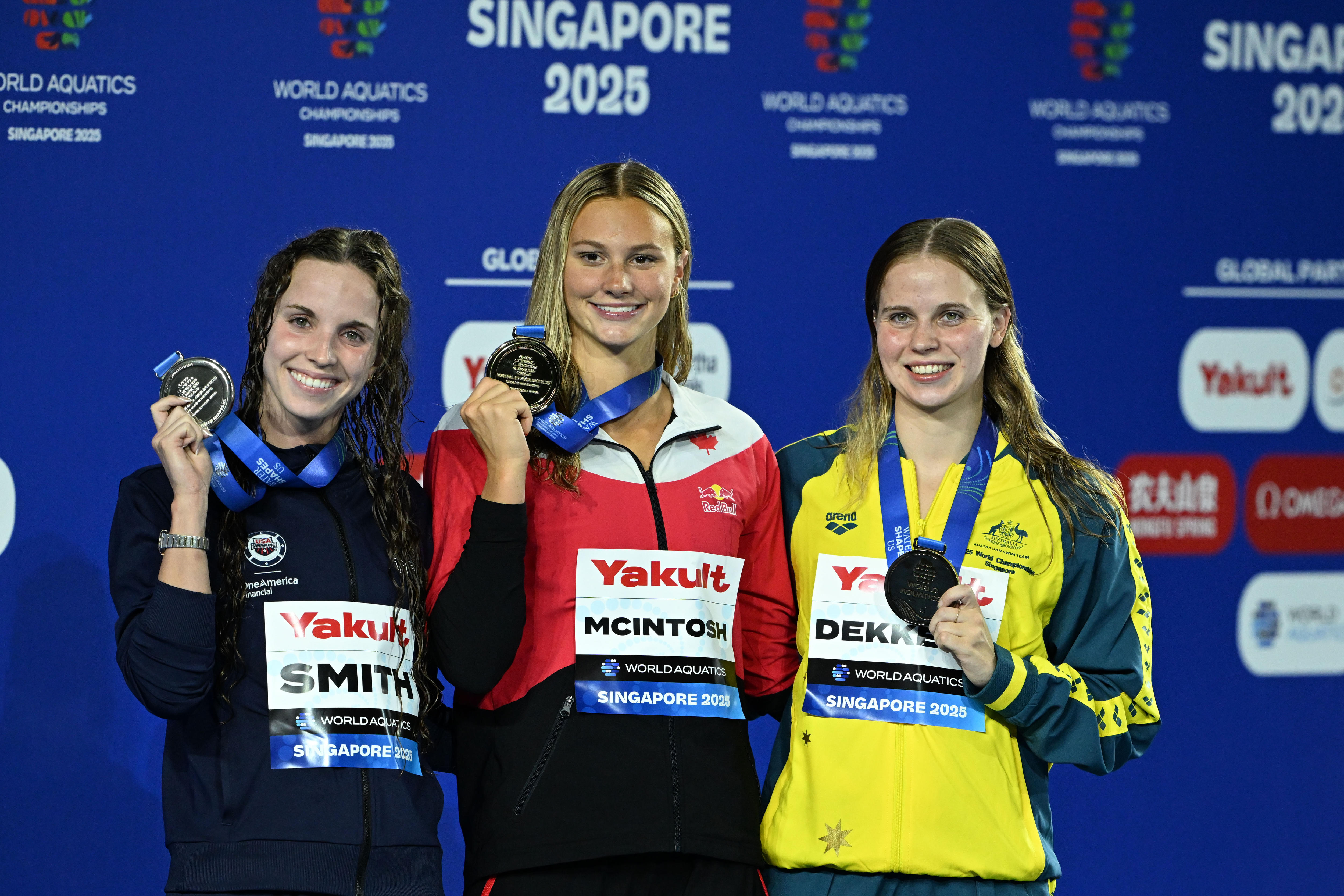 Lizzie Dekkers, Summer McIntosh and Regan Smith show their medals on the podium.