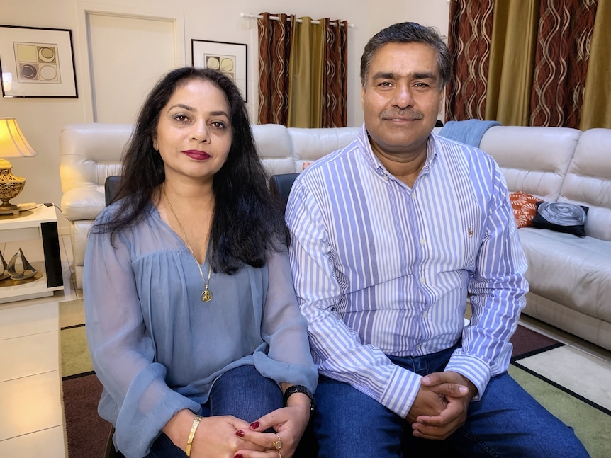 A woman and a man sit side-by-side on a couch, smiling.