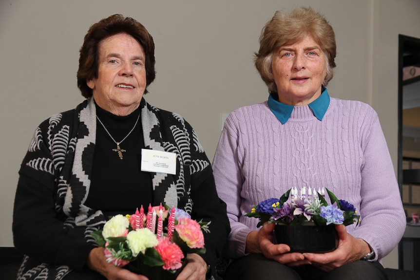 Two women sitting holding floral arrangements with candles in them