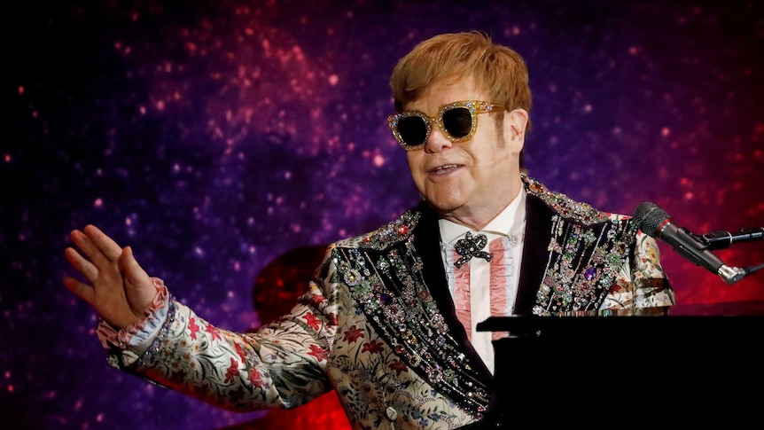 Singer Elton John performs on stage sitting at a piano