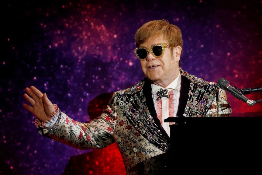 Singer Elton John performs on stage sitting at a piano