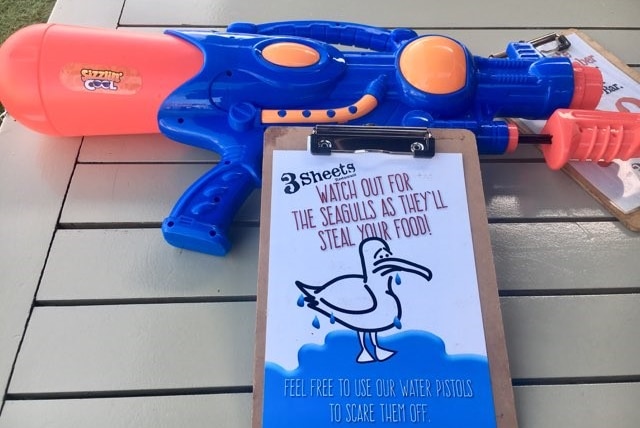 A blue and red water gun on a cafe table with a notice saying it can be used against seagulls.