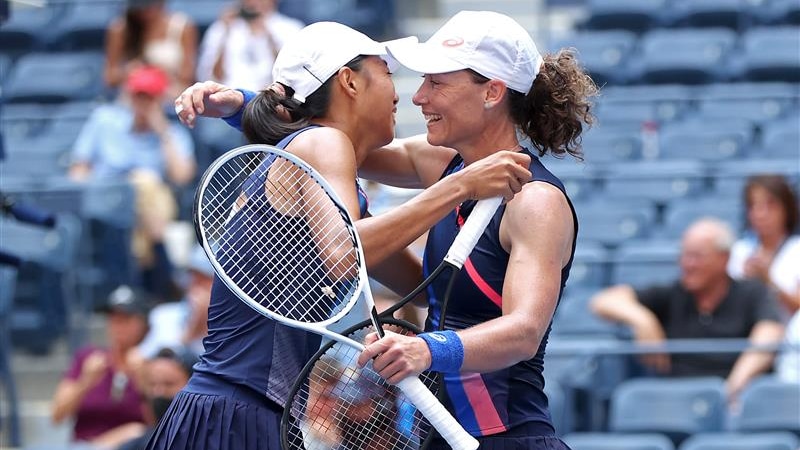 Two smiling women's doubles players embrace, with Sam Stosur holding her racquet in one hand after winning the US Open.