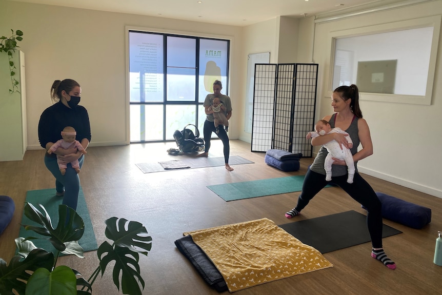 Three women do yoga with babies in their arms.