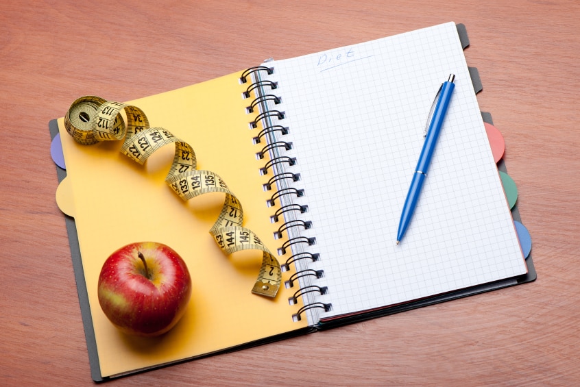 Tools for goal setting - notepad and pen, tape measure and apple