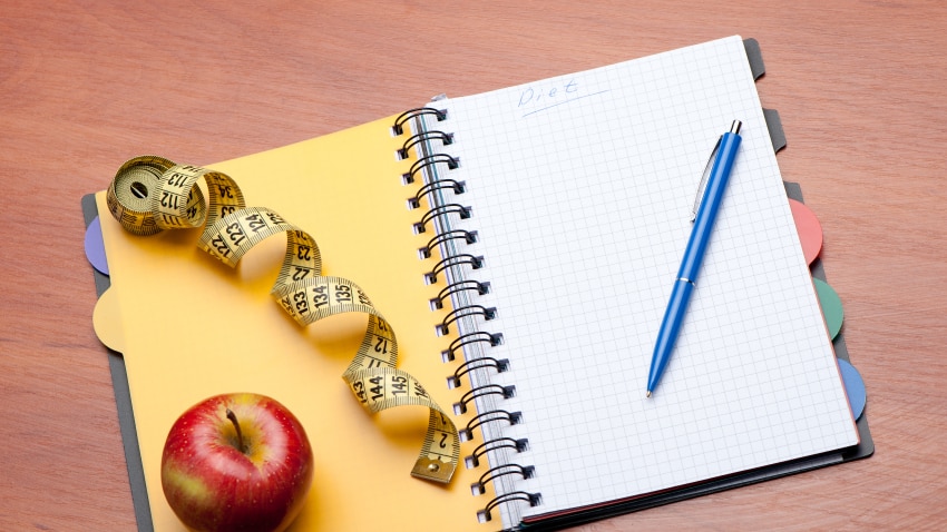 Tools for goal setting - notepad and pen, tape measure and apple