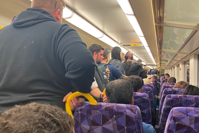 lots of commuters pack into a train carriage, there are lots of people standing in the aisle.