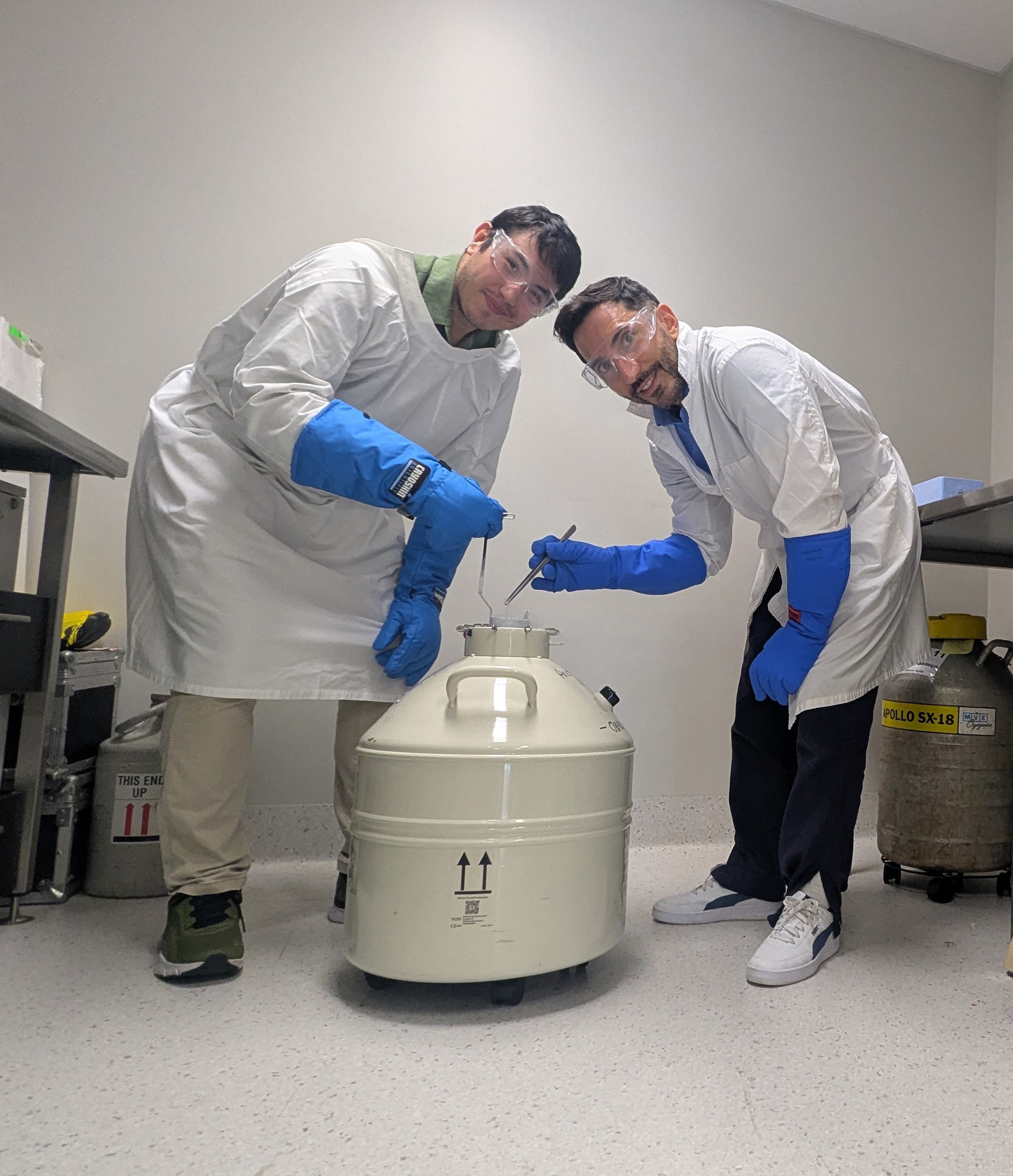 two male scientists with blue globes standing over a white tank