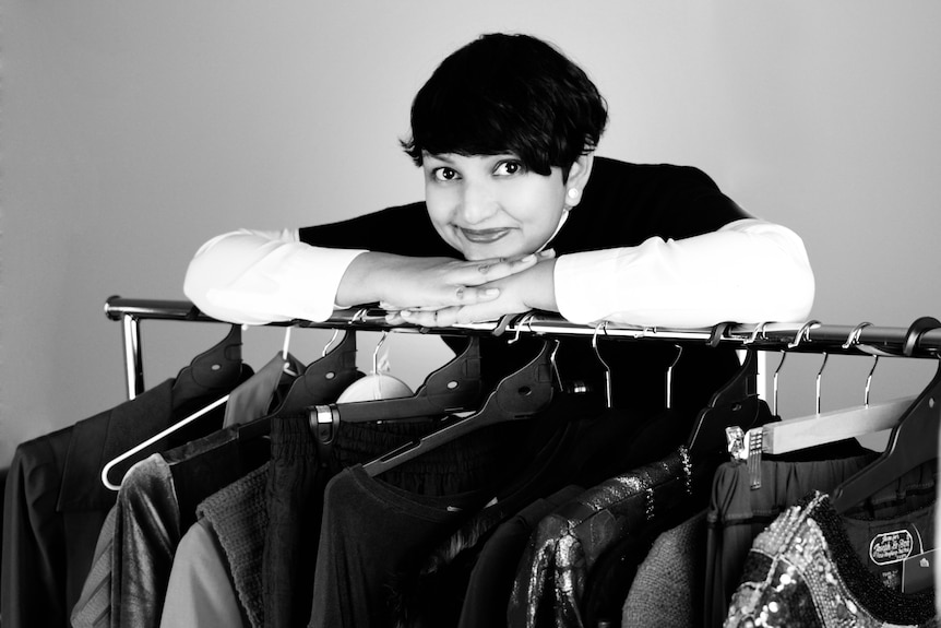 A woman leans on a coat rack.