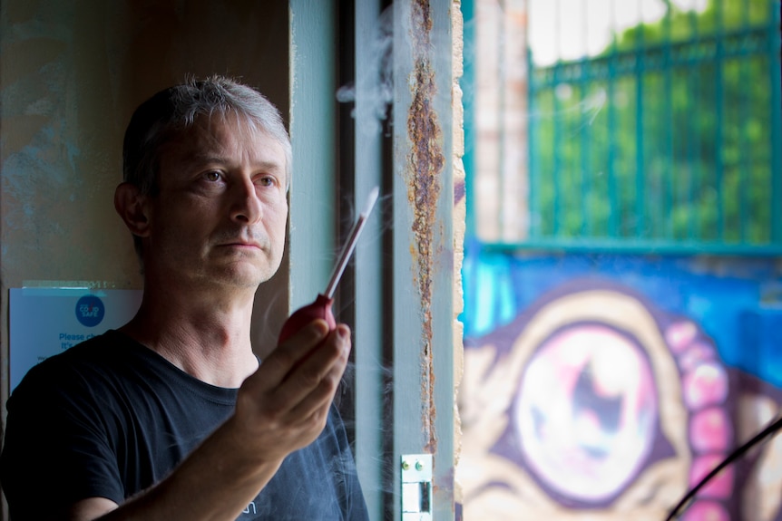 Andrew Orfanos looks at smoke coming out of a smoke tube as he stands in a doorway.