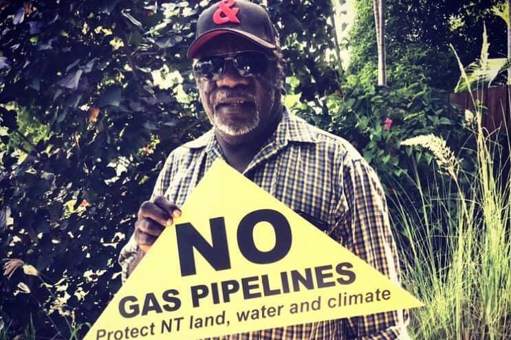 An Indigenous man holding a sign saying 'No Gas Pipelines - Protect NT Land, Water and Climate'