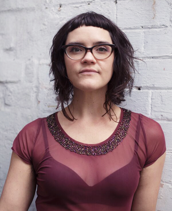 A woman stands against a white brick wall.