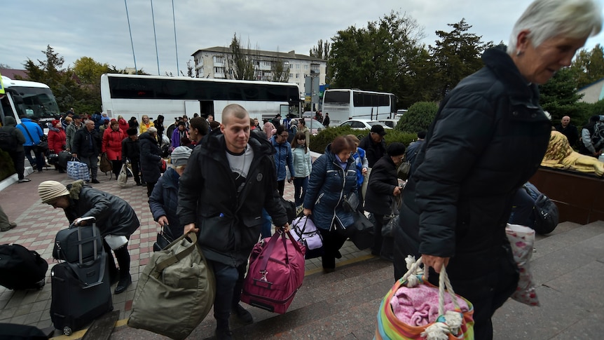 People carrying luggage make their way up stairs from buses towards a train station.