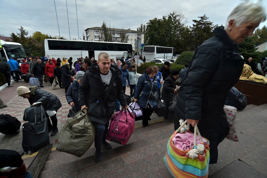 People carrying luggage make their way up stairs from buses towards a train station.