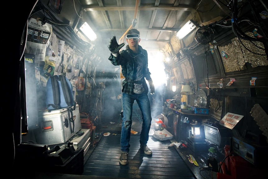 Colour still image of Tye Sheridan wearing a virtual reality headset, standing in a van like set in 2018 film Ready Player One.