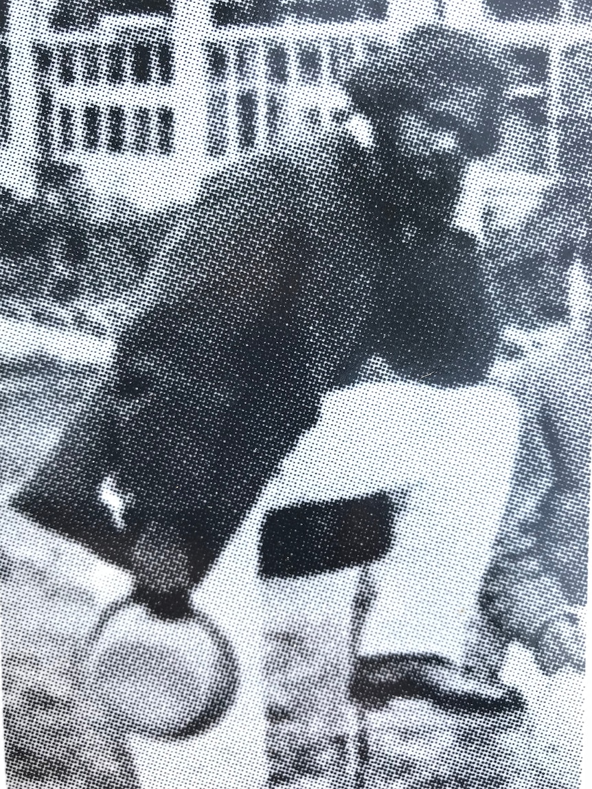 Man wearing white pants and a dark coat, poses with my leg lifted on a stool and a bowler hat in hand.