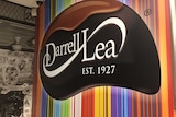 Photo of a wall or large sign with the words Darrell Lea Est. 1927 written on a dark brown bean shape against rainbow background