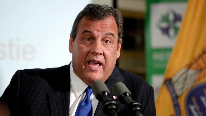 Chris Christie is seated and speaking into microphones during a news conference