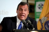 Chris Christie is seated and speaking into microphones during a news conference