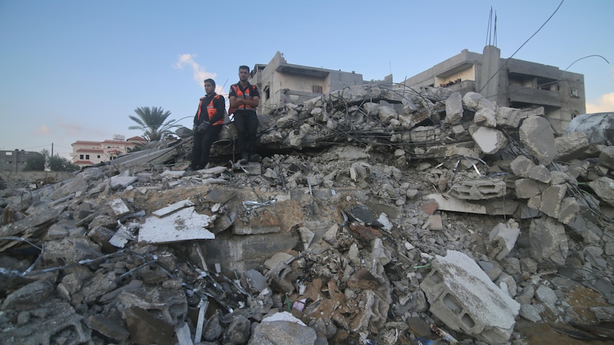Palestinian rescue service members sit on the rubble of a building destroyed in an Israeli airstrike.