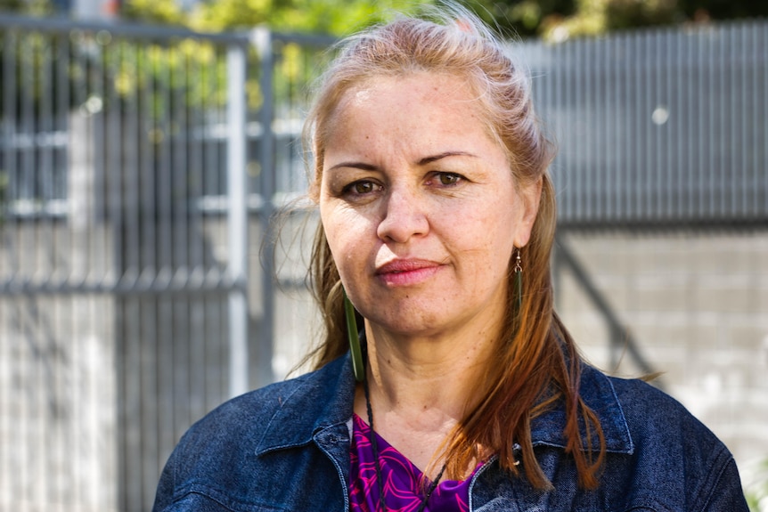 A Maori woman with dark features but lighter blonde hair with a thoughtful facial expression standing outside