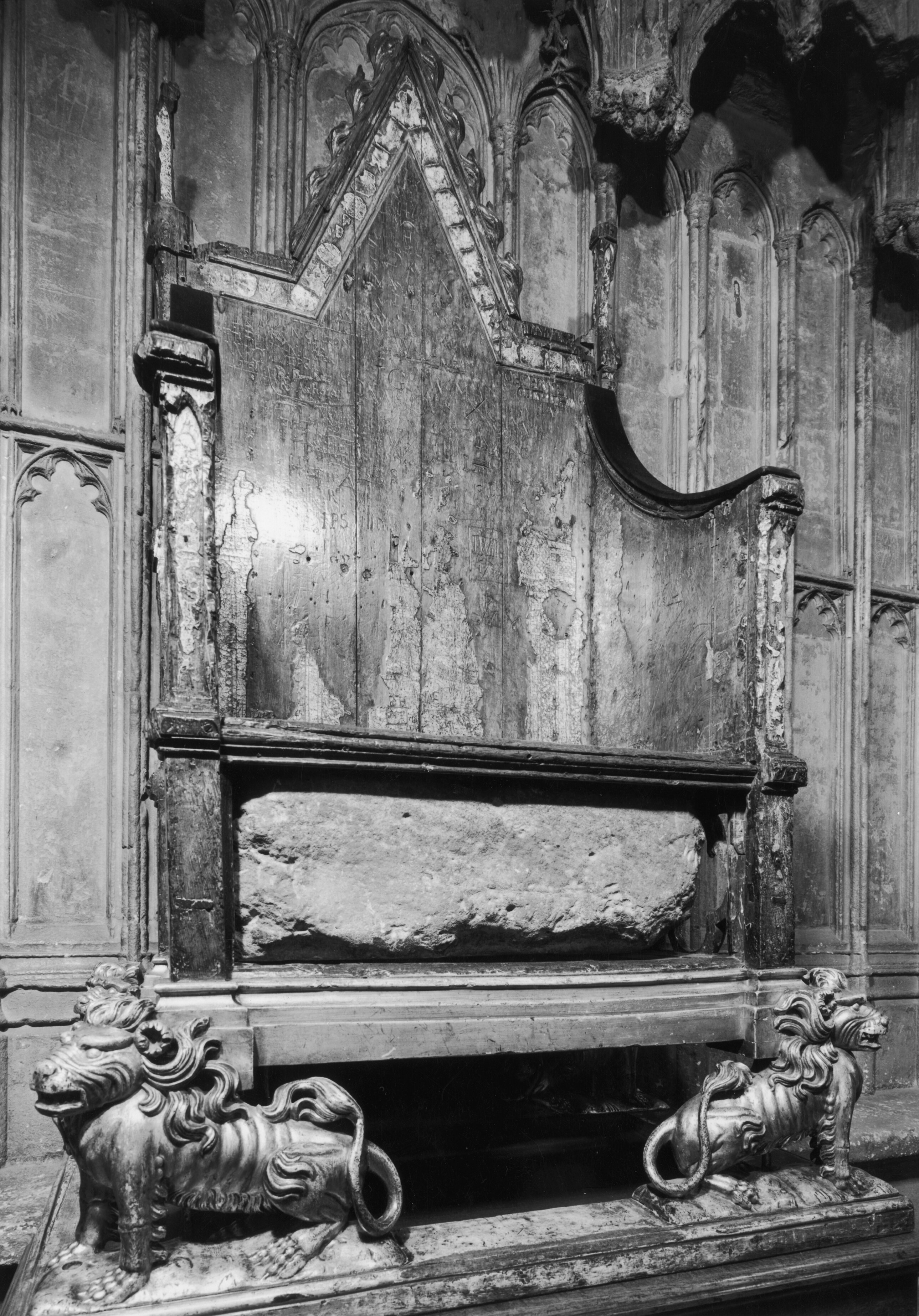A black and white photo of a large block of stone embedded in a grand-looking wooden seat. 