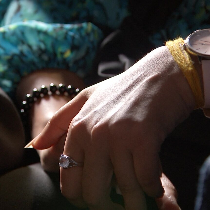 A woman's hands resting in her lap. She's wearing rings, bracelets and a watch