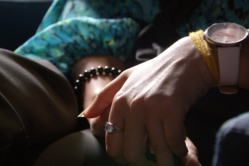 A woman's hands resting in her lap. She's wearing rings, bracelets and a watch