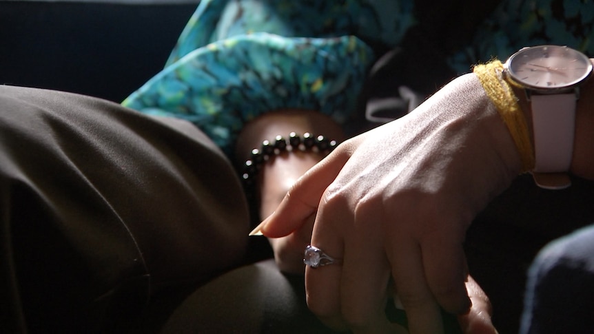 A woman's hands resting in her lap. She's wearing rings, bracelets and a watch