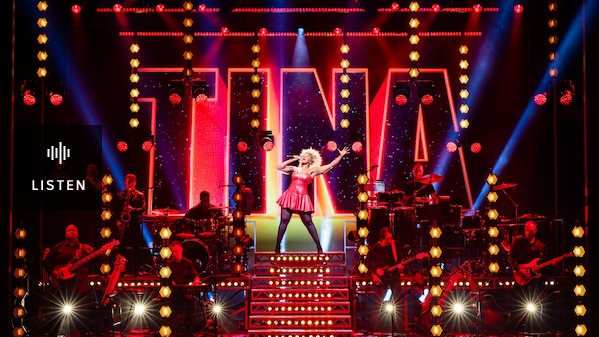 On stage in front of a sign that says TINA and flanked by a band, a black woman stands at the the top of a staircase singing. Has Audio