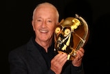 Anthony Daniels smiles holding up a gold light-up robotic looking head.