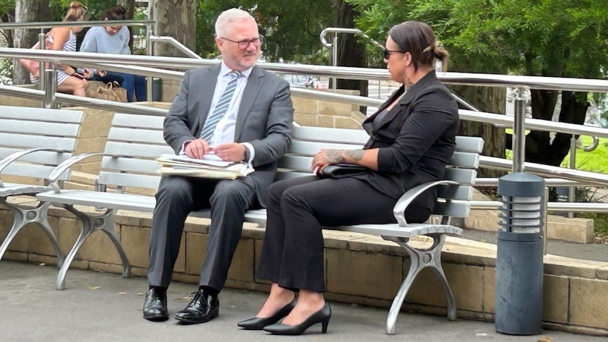A man and woman sit on an outside bench