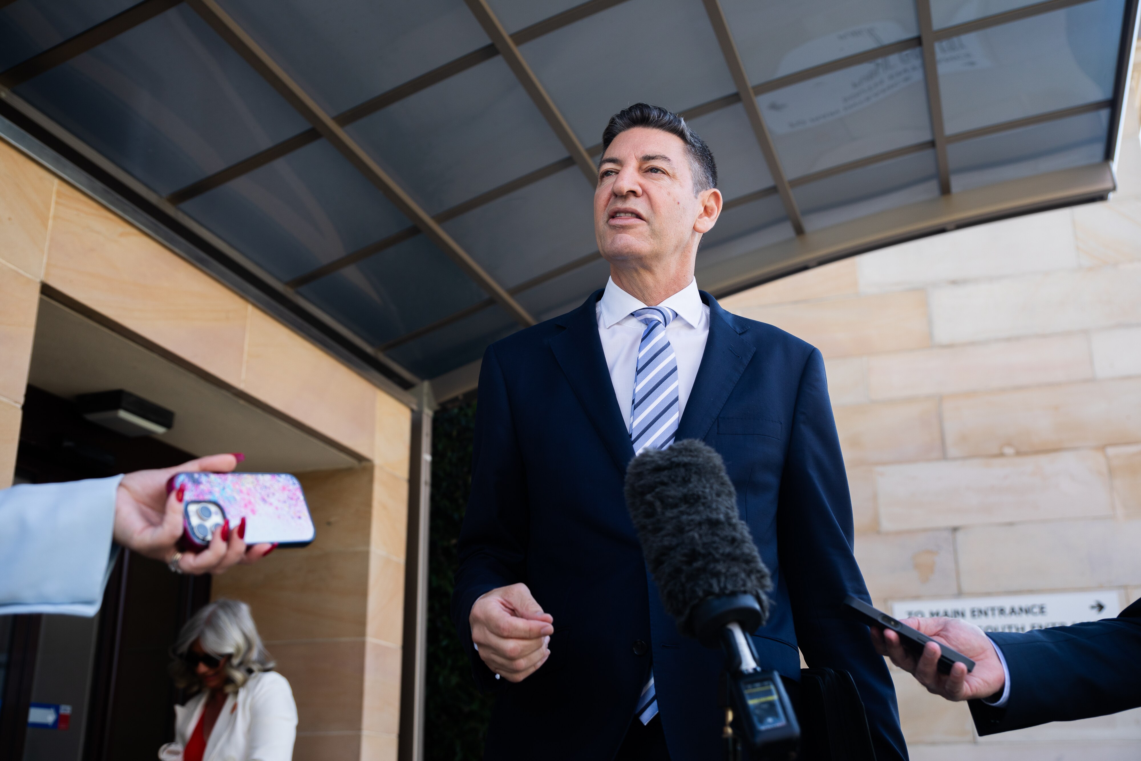 Basil Zempilas habla frente a un micrófono frente a un edificio.