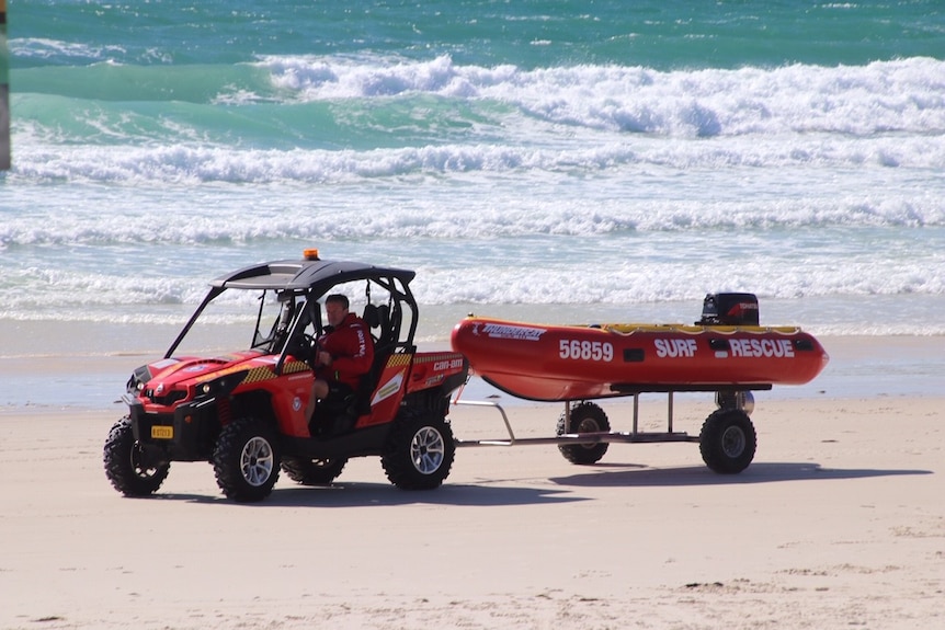 A red surf rescue buggy tows an inflatable boat along a beach.