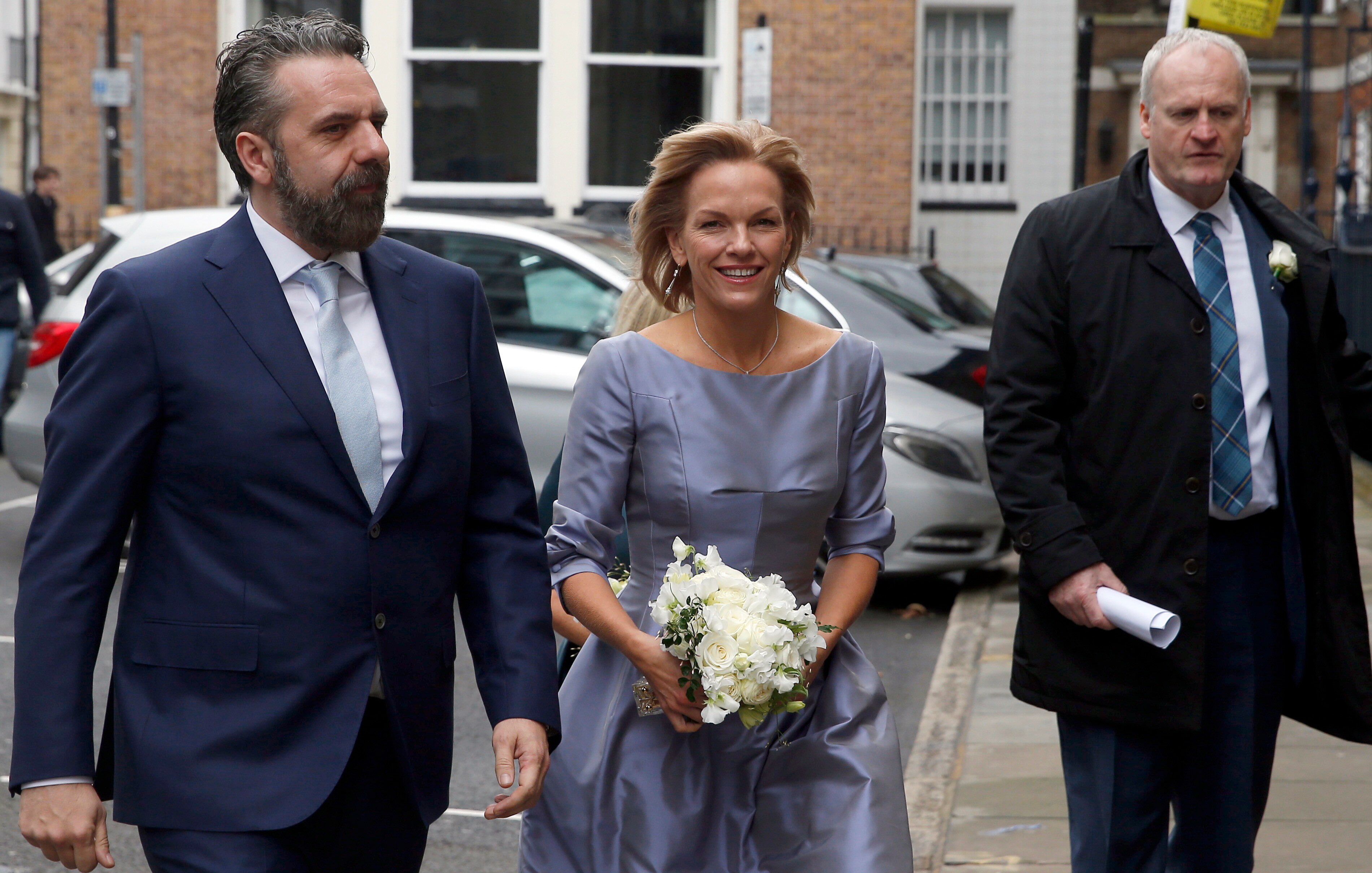 Elisabeth Murdoch in a blue dress, clutching a bouquet of white flowers
