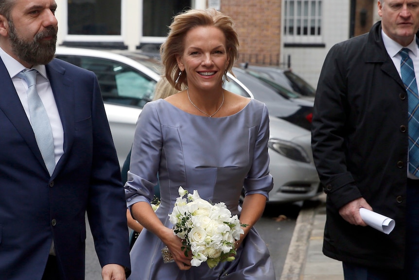 Elisabeth Murdoch in a blue dress, clutching a bouquet of white flowers