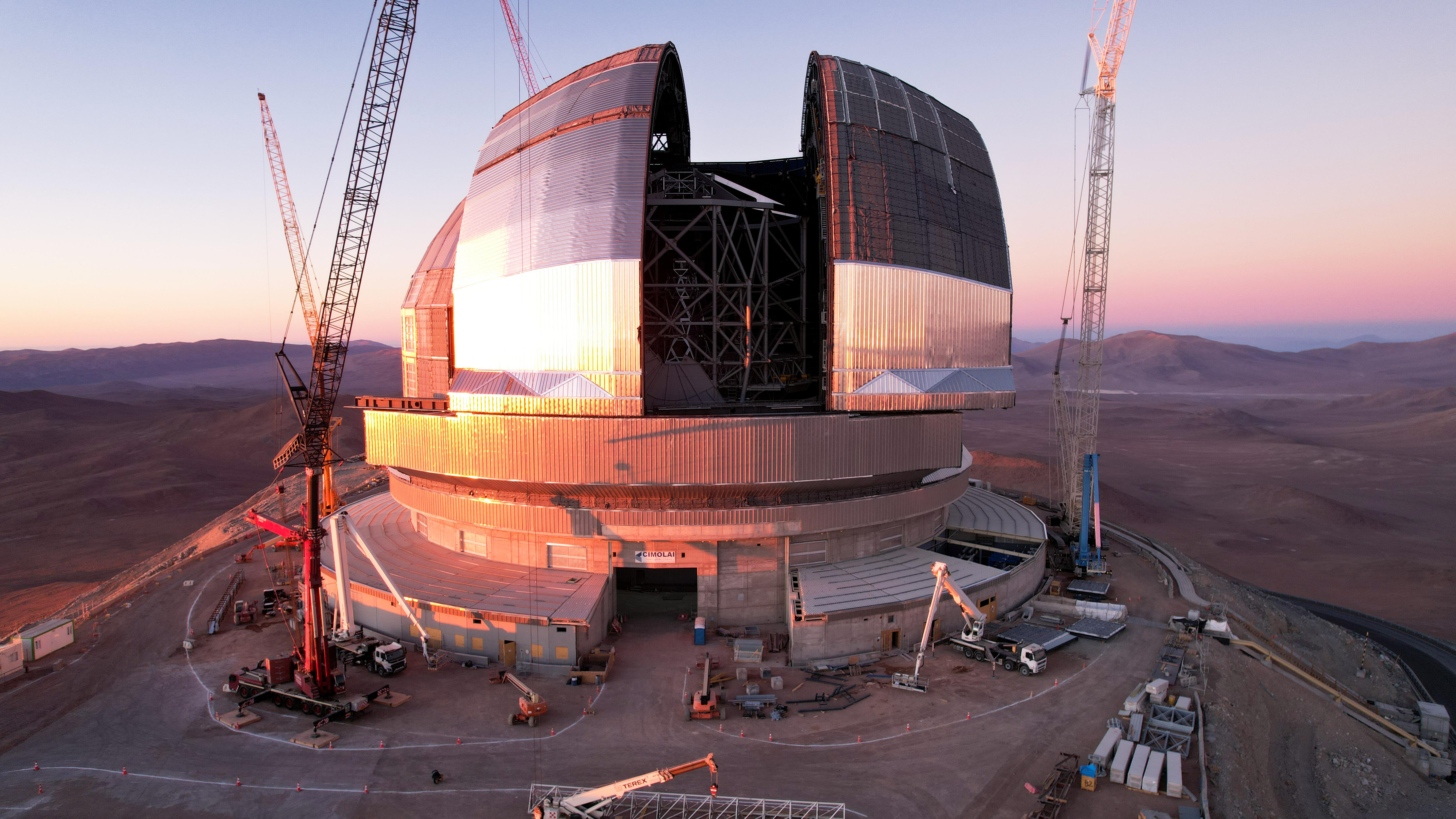 Dome-shaped building surrounded by cranes on a desert mountaintop.